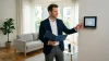 Homme en costume montrant thermostat dans salon moderne