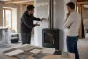 Un installateur conseille un propriétaire devant un poêle éteint et des échantillons de finition.